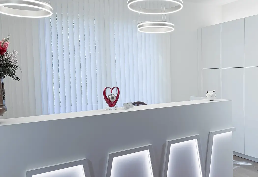 Moderner, weißer Empfangstresen der Praxis Boyraz mit LED-Beleuchtung, einer roten Herz-Skulptur und weißen Lamellen im Hintergrund.